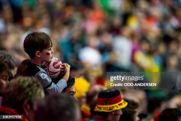 Young handball fan clutches a ball as he follows the action during the IHF Men's World Championship 2019 Group A handball match between Germany and...