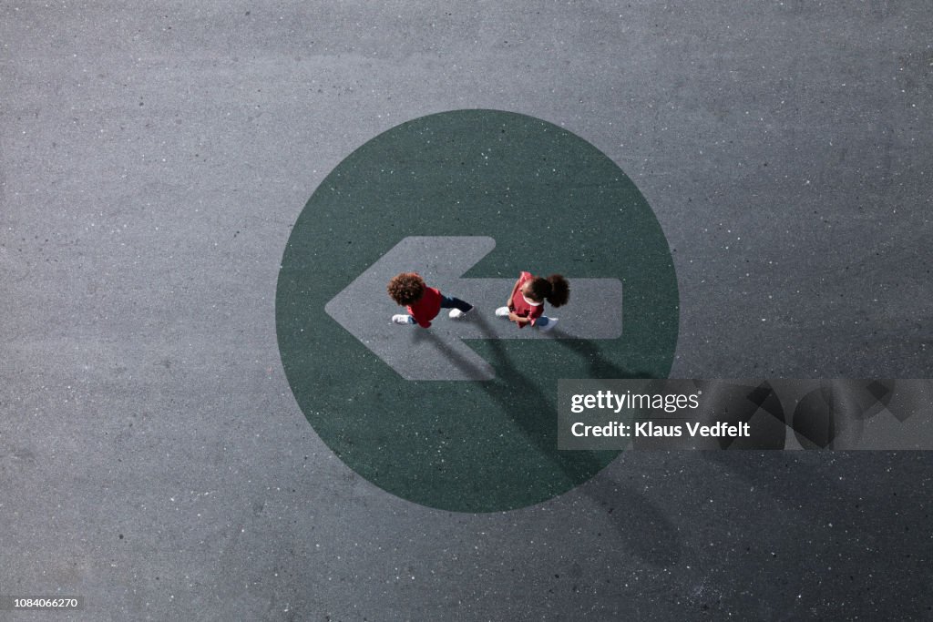 School children dressed in red, walking across painted circle with arrow