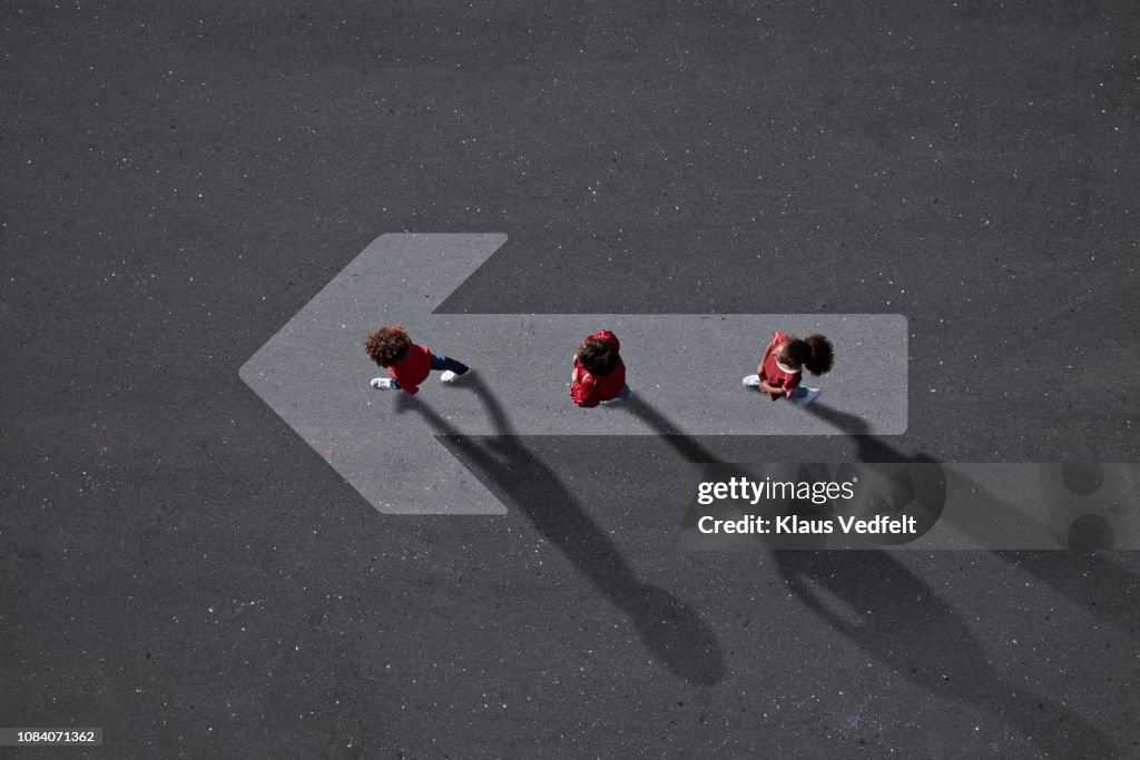 School children dressed in red, walking across big painted arrow