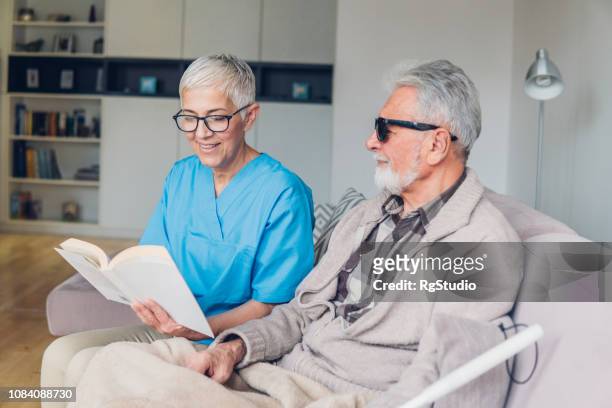 happy nurse reading to blind patient - blind man stock pictures, royalty-free photos & images