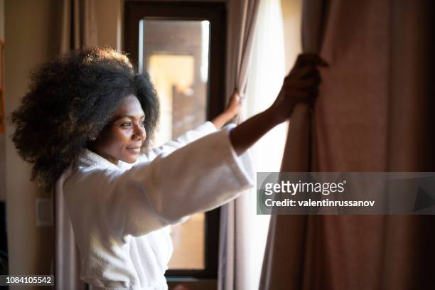 woman pulling curtains in hotel room - black curtain stock pictures, royalty-free photos & images