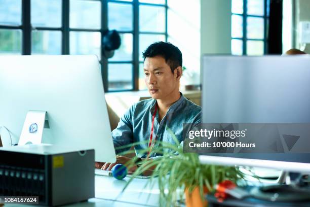 mid adult man using computer and concentrating - asian man sitting casual imagens e fotografias de stock