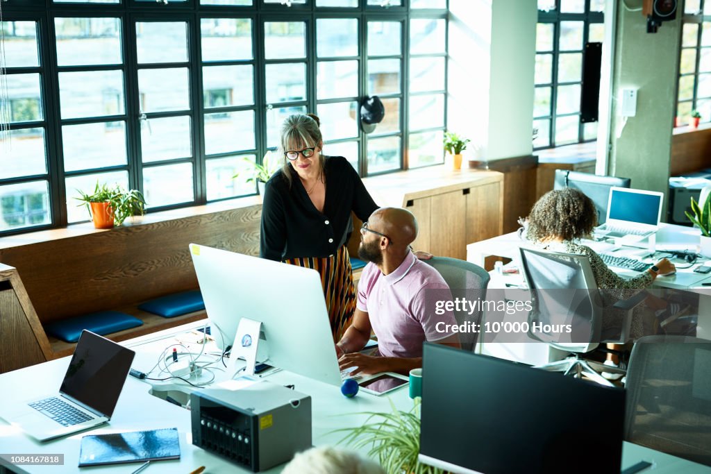 Female manager chatting to male colleague at work station