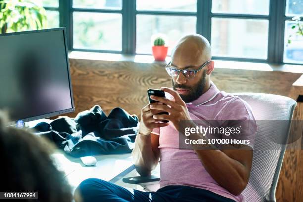 mid adult man with beard and glasses texting in office - perder el tiempo fotografías e imágenes de stock