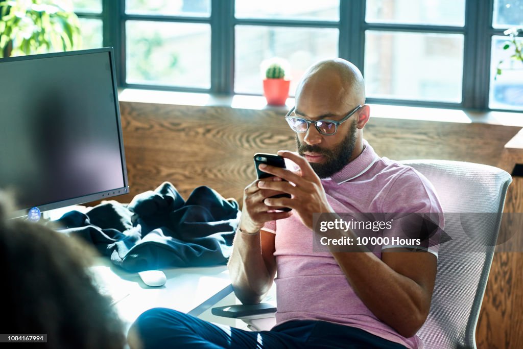 Mid adult man with beard and glasses texting in office