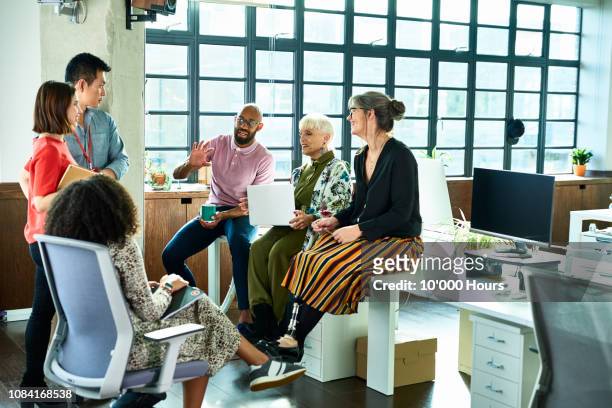 business colleagues in meeting with female amputee sitting on desk - werkplek stockfoto's en -beelden