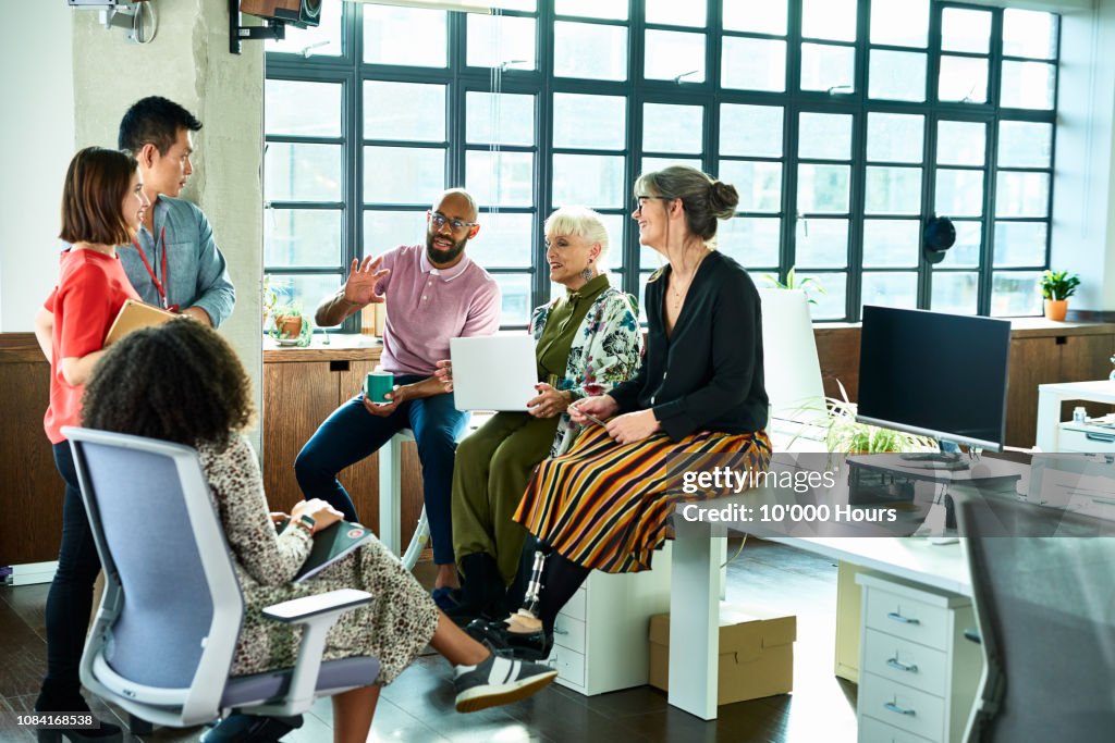 Business colleagues in meeting with female amputee sitting on desk