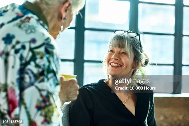 cheerful mature woman smiling and chatting with colleague - friends chatting mature foto e immagini stock