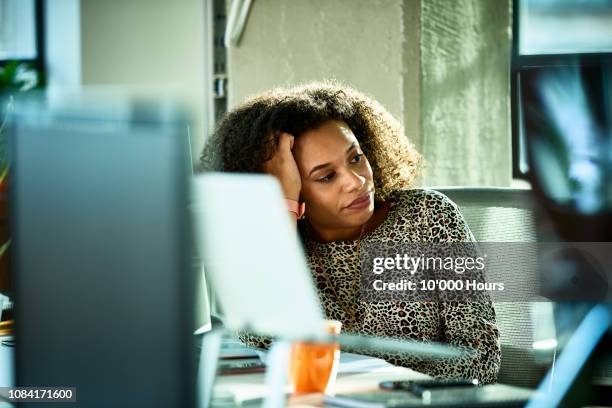 portrait of mixed race woman looking bored at desk - stress au travail photos et images de collection