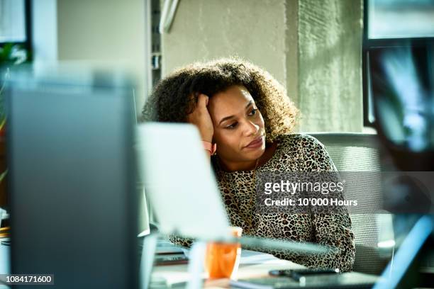 portrait of mixed race woman looking bored at desk - frustrazione foto e immagini stock