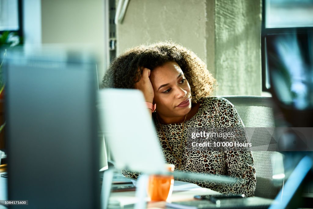 Portrait of mixed race woman looking bored at desk