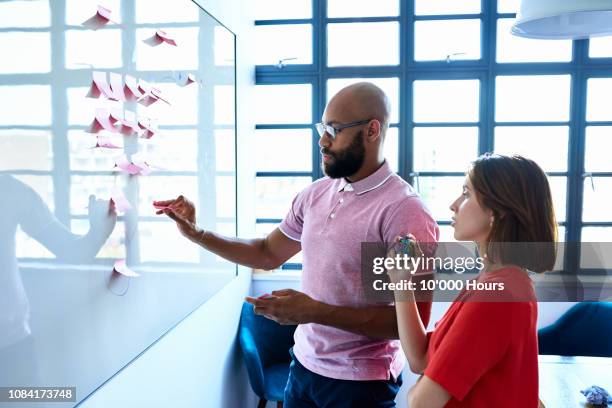 young woman and male colleague writing ideas on adhesive notes - processes fotografías e imágenes de stock