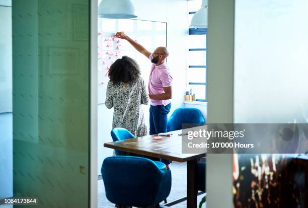male and female colleagues brainstorming with adhesive notes on whiteboard - platzieren stock-fotos und bilder