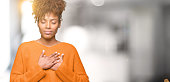 Beautiful young african american woman over isolated background smiling with hands on chest with closed eyes and grateful gesture on face. Health concept.