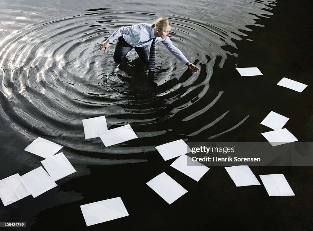 Businessman in water gathering floating paperwork