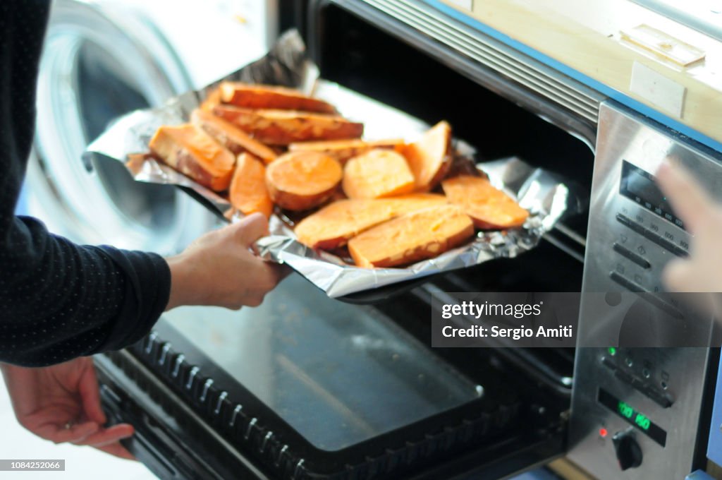 Putting a tray of sweet potatoes in the oven