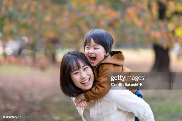 若い母親と息子は一緒に公園で遊ぶ - おんぶ ストックフォトと画像