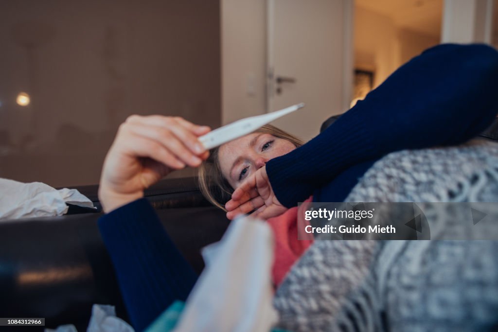 Ill woman looking at thermometer.