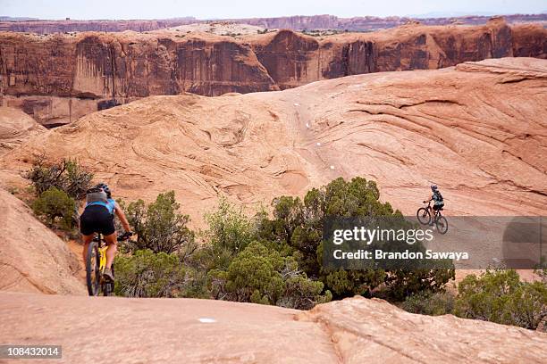 two women mountain bike one of the slick rock routes in moab utah. - slickrock trail stock pictures, royalty-free photos & images