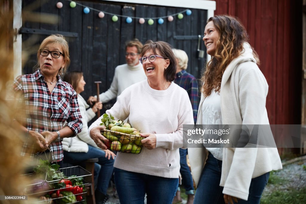 Cheerful women standing with baskets against friends at farm during dinner party