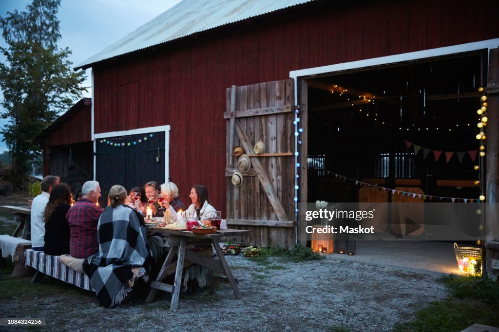 Male and female friends enjoying dinner party against barn at farm