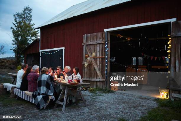 Female and male friends enjoying dinner party against barn at farm