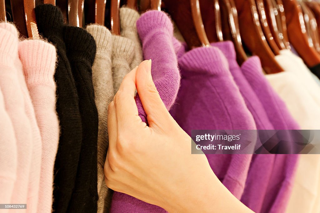 Hand touching cashmere sweater on clothing rack