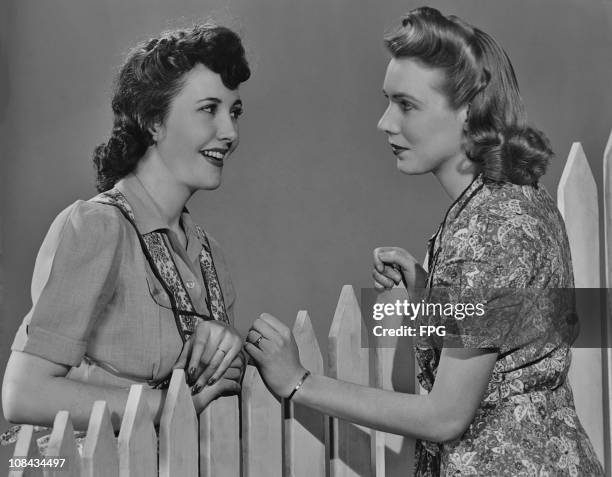 Two women neighbours talking over a white picket fence in the 1940's.