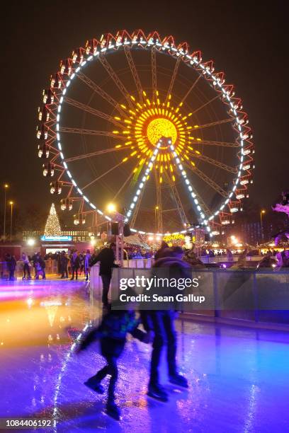 Visitors ice skate as an illuminated ferris wheel spins behind at the annual Christmas market at Alexanderplatz on December 2, 2018 in Berlin,...