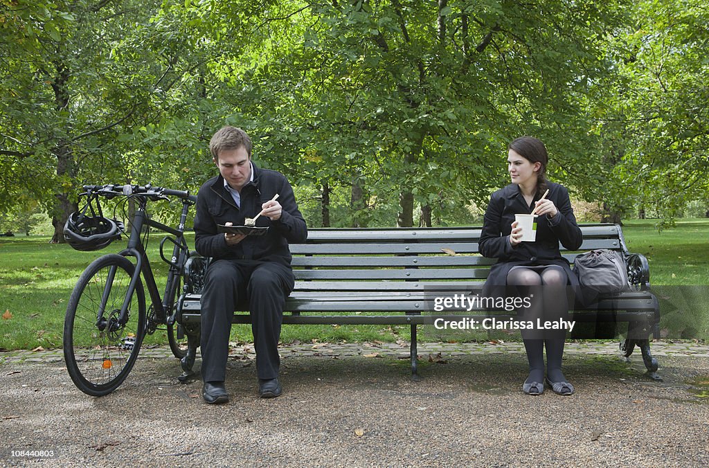 Woman and man eating lunch on park bench