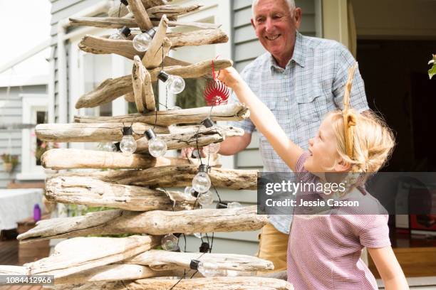 child putting on christmas decorations on tree with grandfather - new zealand christmas stock pictures, royalty-free photos & images