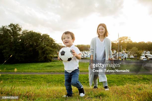 son who plays with soccer ball, mother watching over. - football for hope stock-fotos und bilder