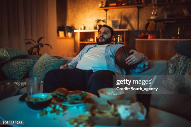 mollige man kijken een basketbal wedstrijd op de bank - basketball match on tv stockfoto's en -beelden