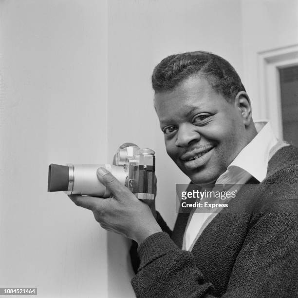 Canadian jazz pianist and composer Oscar Peterson holding a camera, UK, 22nd February 1963.