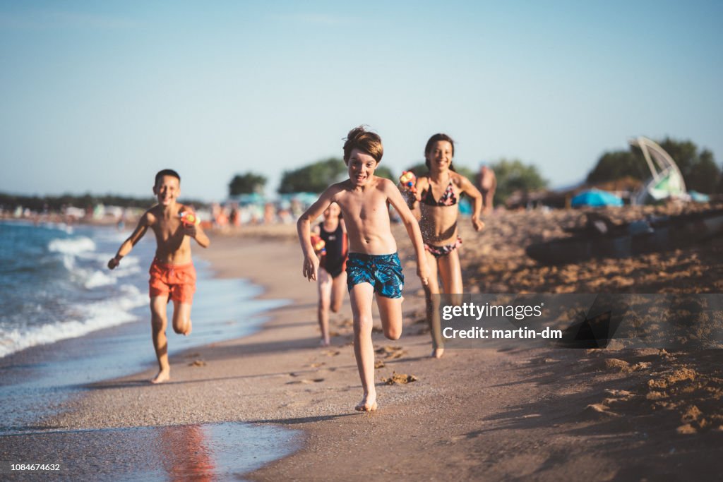 Kinder laufen und schießen mit Wasserpistolen am Strand