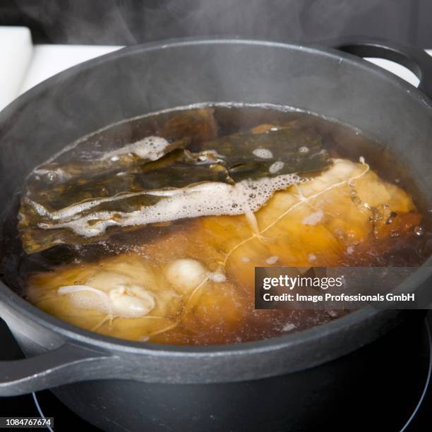 cooking the seitan roll in a cooking pot of water and soya sauce - seitan foto e immagini stock