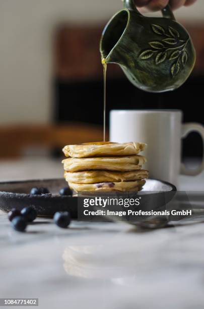 syrup pouring from a jug onto a pile of pancakes - syrup stockfoto's en -beelden