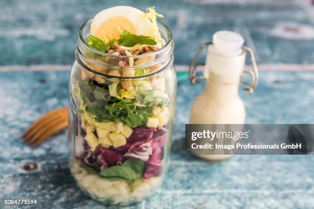 orzo pasta with lambs lettuce, radicchio, endive, croutons, cheese, walnuts and eggs in a glass jar with dressing and a wooden fork - krulandijvie stockfoto's en -beelden