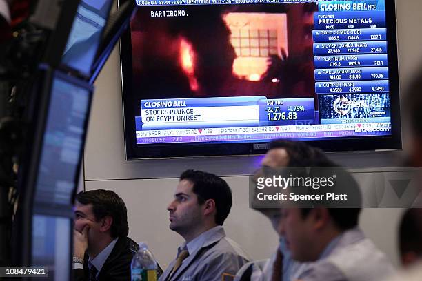 With a television screen showing images of the unrest in Egypt, traders work on the floor of the New York Stock Exchange at the end of the trading...