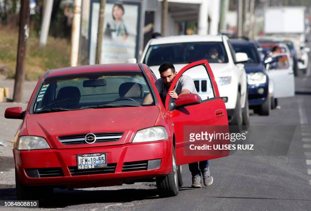 Man pushes his car as he queues at a Pemex service station in Tlajomulco, Jalisco State, Mexico, on January 18, 2019 as a controversial government...