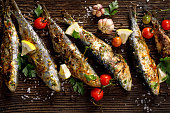 Fried fishes with addition of herbs, spices and lemon slices on a wooden background.