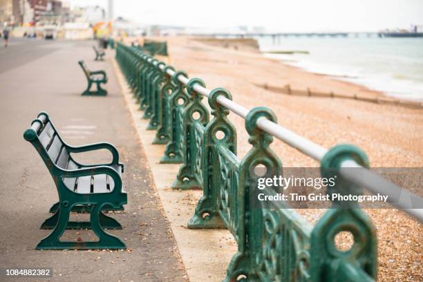 an empty green bench seat and railings, on the promenade, brighton, uk - palace pier fotografías e imágenes de stock
