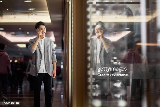 young man talking on mobile phone in luxury mall - smart casual walking stock pictures, royalty-free photos & images