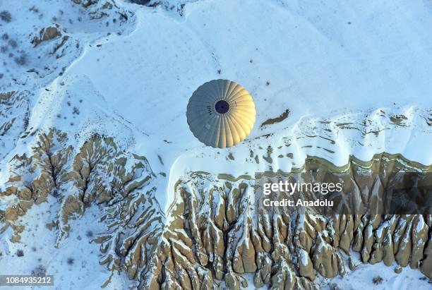 Hot-air balloon glides above fairy chimneys in snow-covered Cappadocia region, located in Central Anatolia's Nevsehir province, Turkey on January 19,...