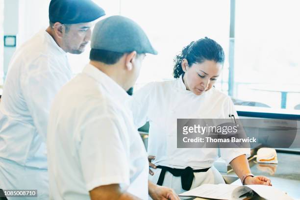 Female chef reviewing plans for dinner service with staff in restaurant kitchen