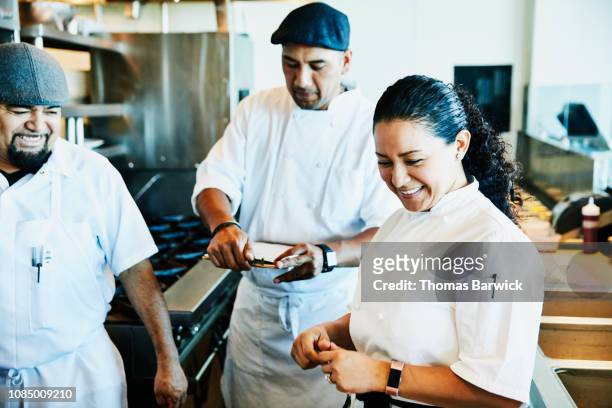 Laughing female chef reviewing plans for dinner service with kitchen staff