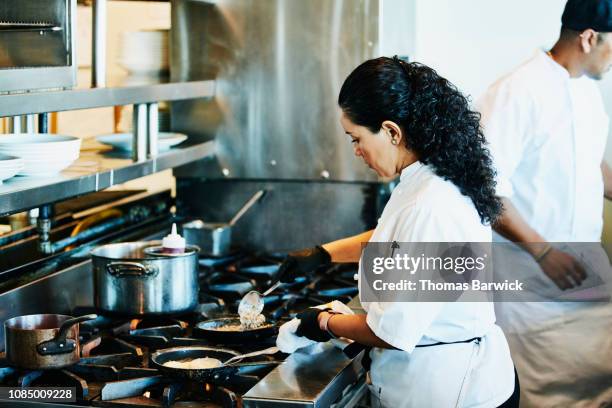 female chef preparing food at stove in restaurant kitchen - stove stock-fotos und bilder