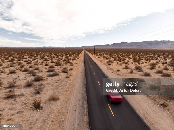 drone view of american car driving in a straight road at the california desert. - route 66 stock-fotos und bilder