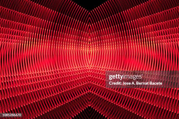 close-up abstract pattern of intertwined colorful light beams of color red color in movement on a black background. - shiny red stock pictures, royalty-free photos & images