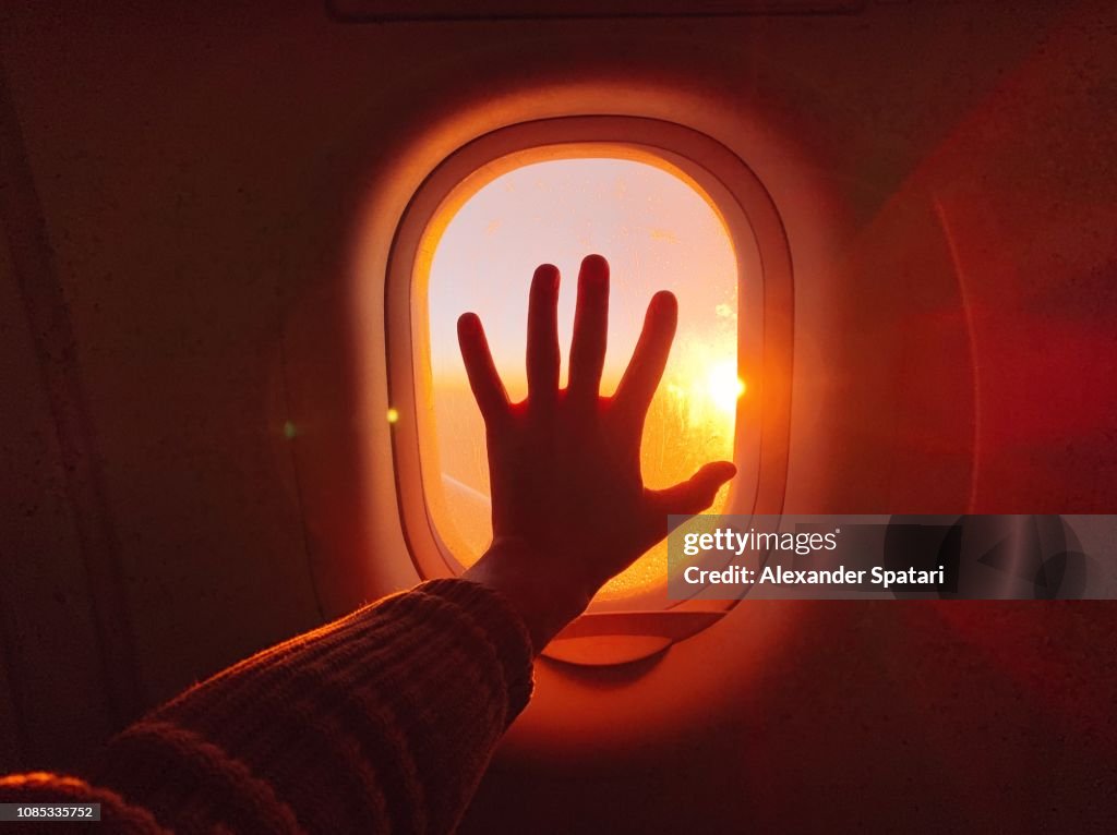 Touching plane window while flying in the sky during sunset